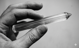 Hand holding a crystal wand against a neutral background