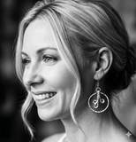 Black and white close-up of a woman wearing silver encircled frond earrings with a blurred background