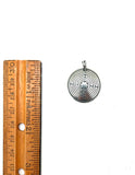 Silver labrynth pendant next to a wooden ruler on a white background