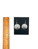 Silver earrings on a black card with a wooden ruler for scale.