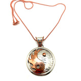 A silver and copper Yin Yang pendant on a red necklace chain.