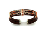 A brown leather cuff bracelet with silver and copper accents, and a flexible brass core.