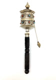 A hand-held prayer wheel with a multicolored geometric pattern on the top and a black handle.